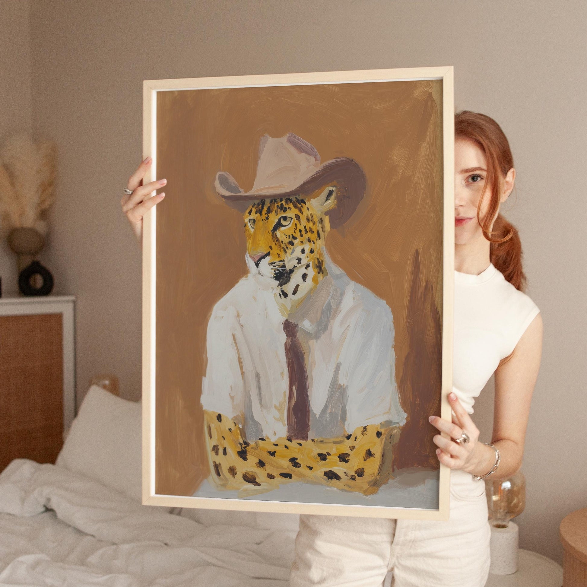 A woman holds up a framed painting of a leopard wearing a cowboy hat.