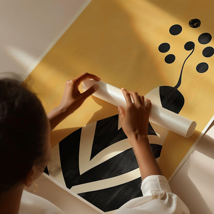 A person's hands are holding a white tube or pipe against a yellow background with a black and white abstract design.