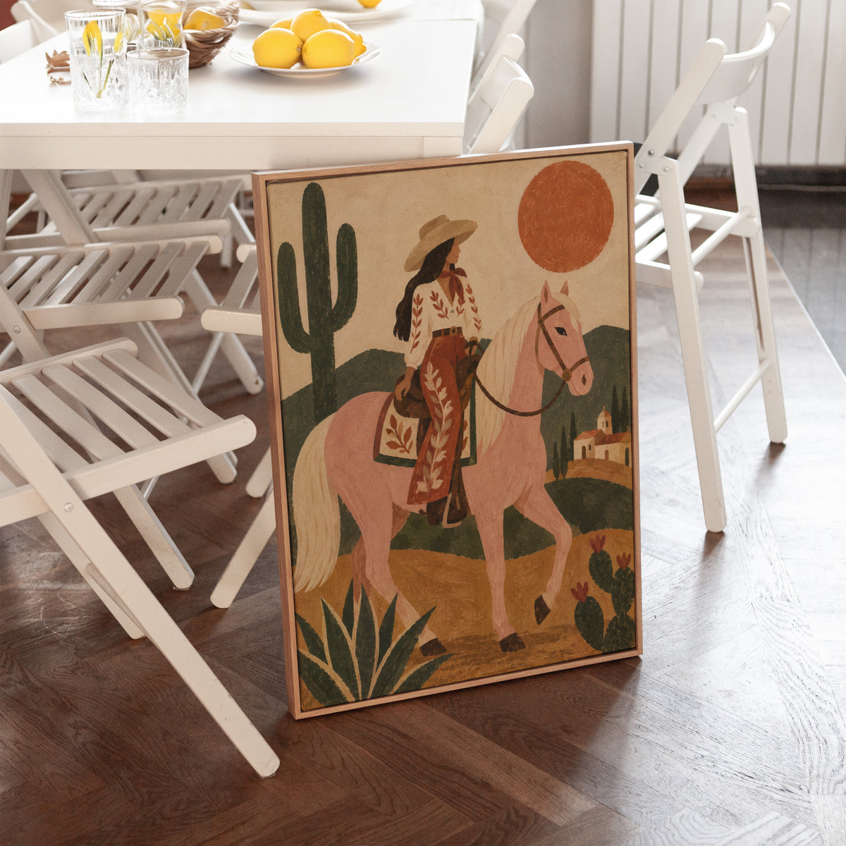 Desert canvas wall art showing cowgirl riding a pale rose horse past cacti under a red desert sun