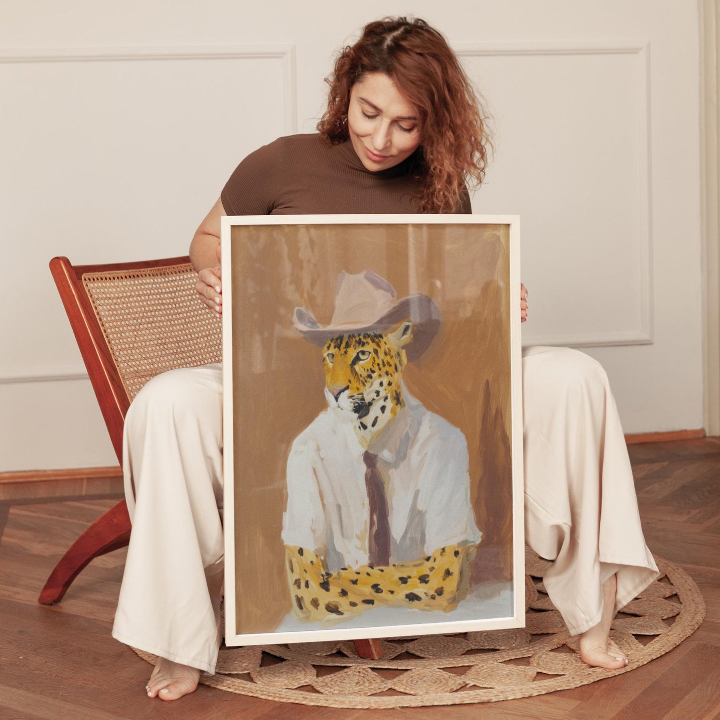 A woman is sitting on a chair, holding a framed painting of a leopard wearing a suit and tie.