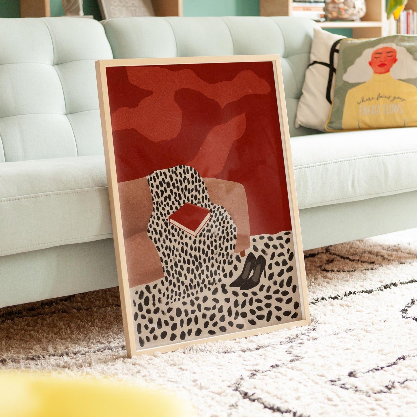 a framed artwork depicting a woman sitting on a couch with a red and black abstract design.