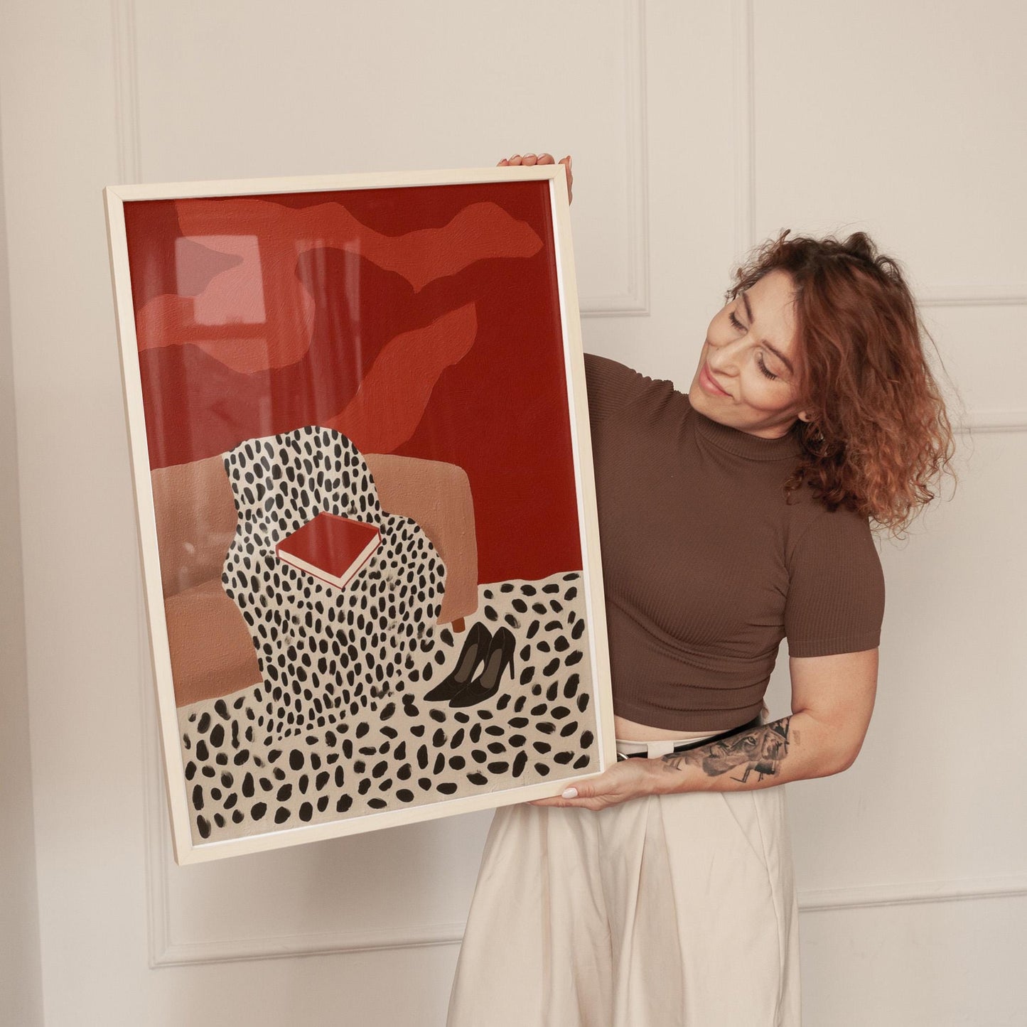 A woman holding a framed artwork with a red background and a black and white spotted pattern.