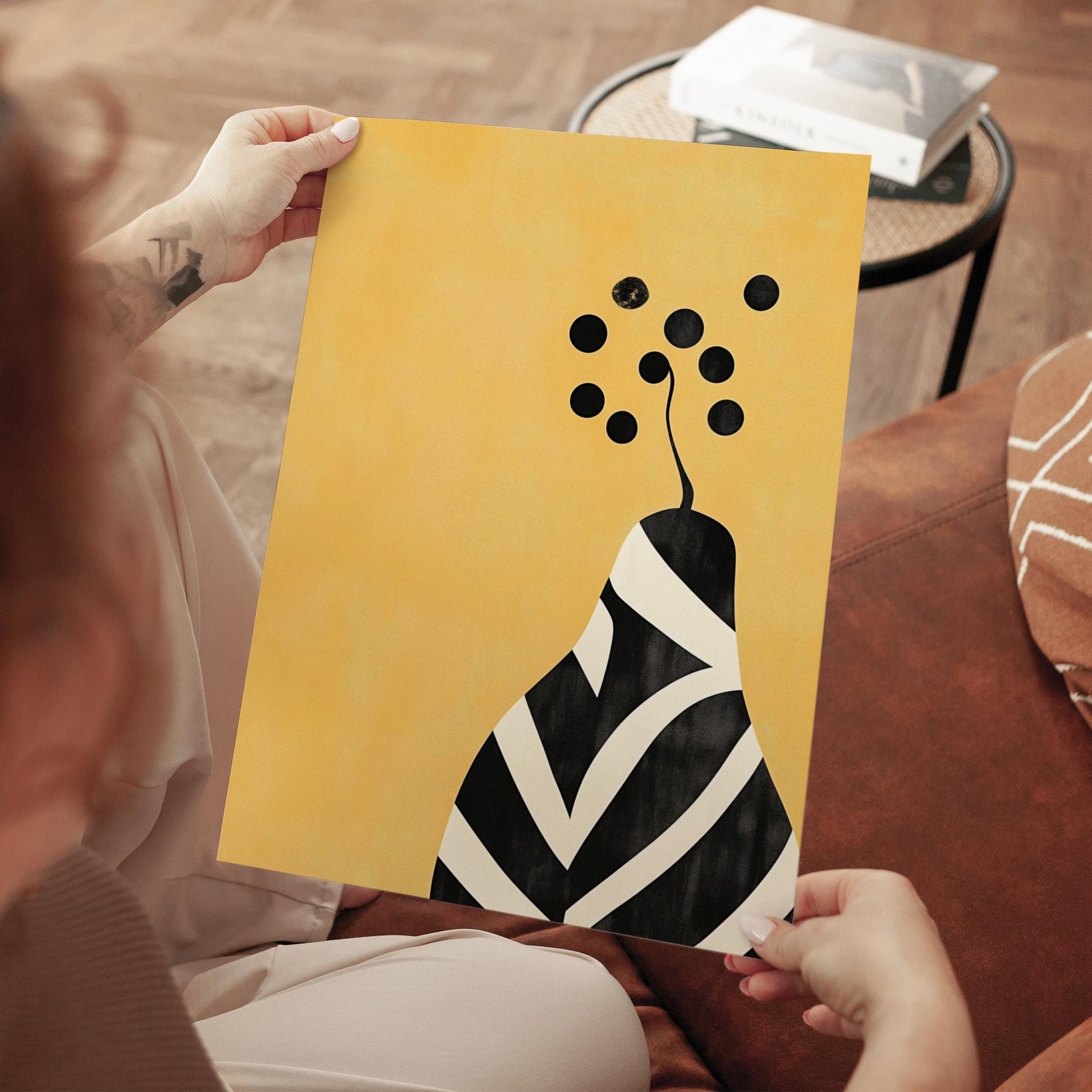 A person is holding a yellow poster with a black and white abstract design featuring a stylized flower or plant-like shape.