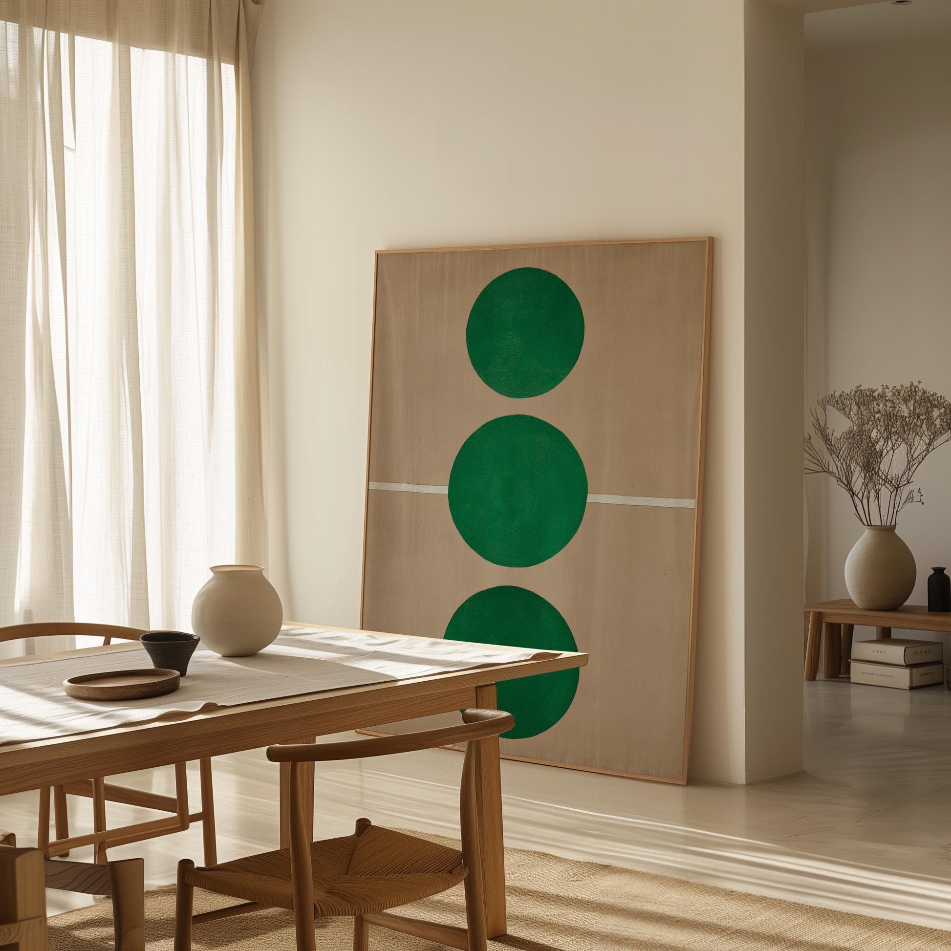a minimalist dining room with a wooden table and chairs, a large abstract painting featuring three green circles on the wall, and a vase of dried flowers on a side table.