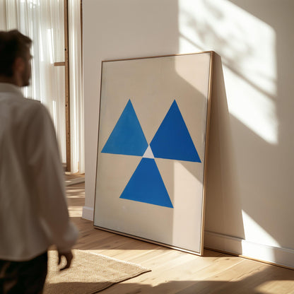 a large framed artwork with a blue triangle design on a white background, displayed in a room with a person walking by.