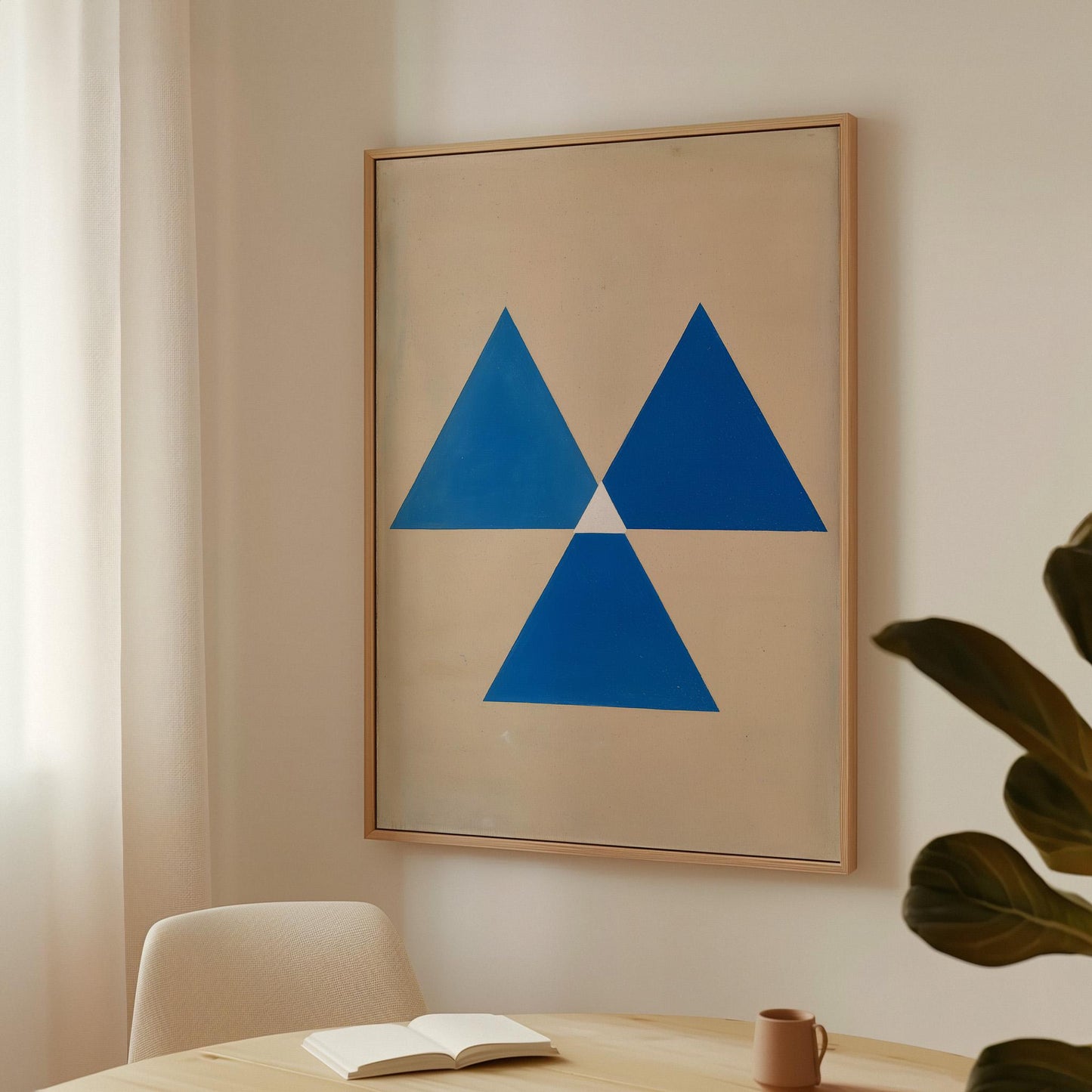 a framed artwork hanging on a wall, depicting a blue triangle design. In the foreground, there is a table with a book and a cup on it, suggesting a cozy and comfortable setting.