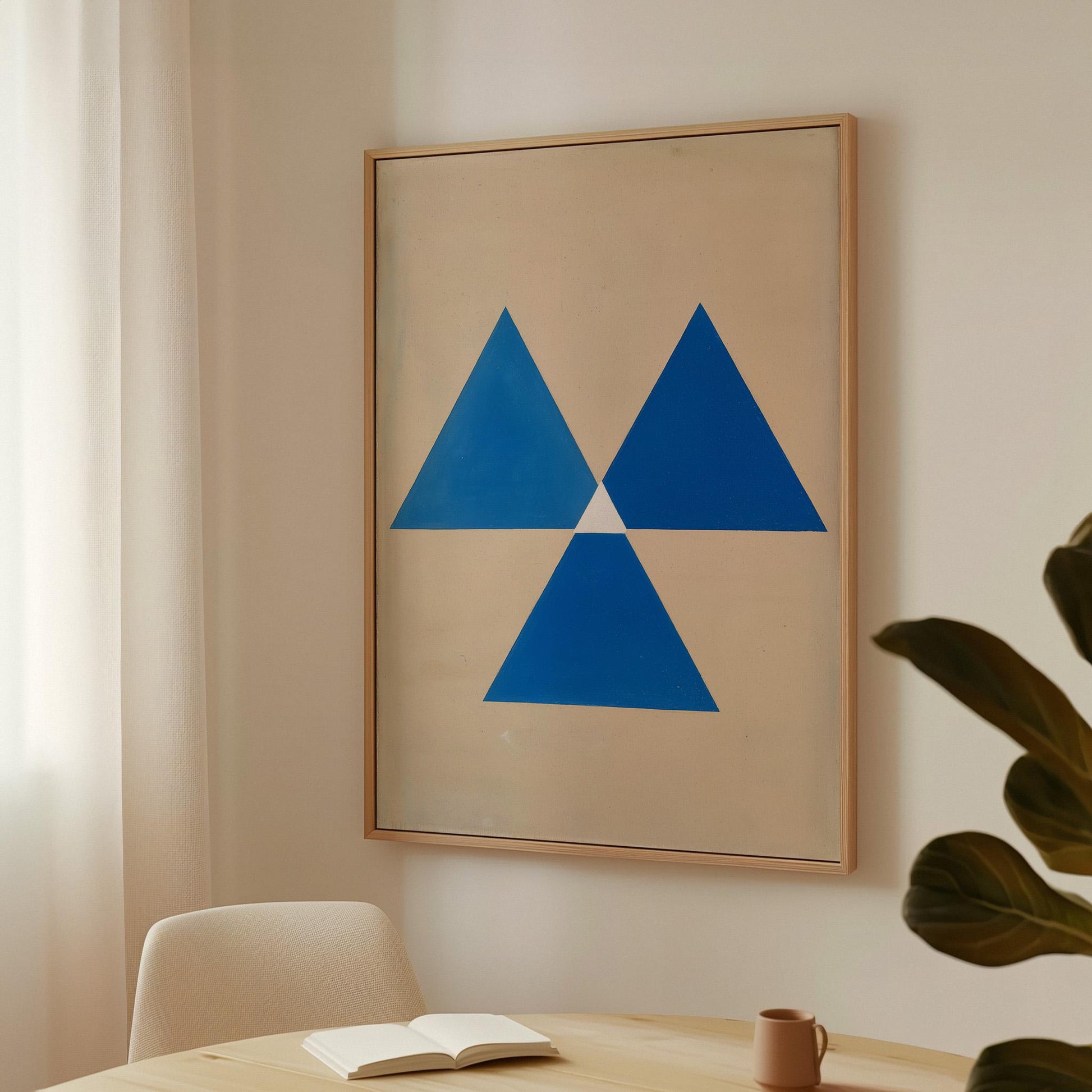 a framed artwork hanging on a wall, depicting a blue triangle design. In the foreground, there is a table with a book and a cup on it, suggesting a cozy and comfortable setting.