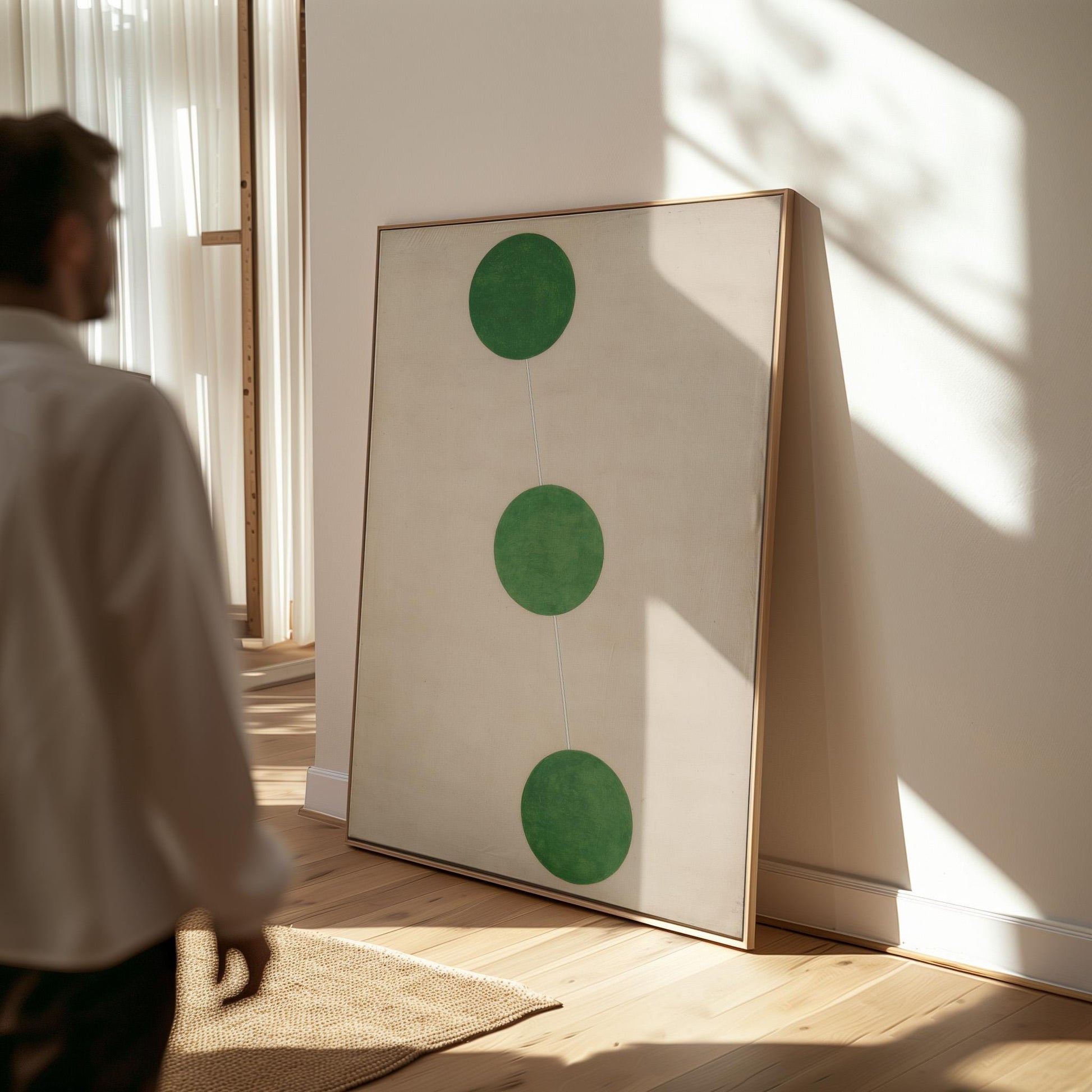 a person standing in a room with a large white painting on the wall, which has three green circles arranged in a triangular formation.