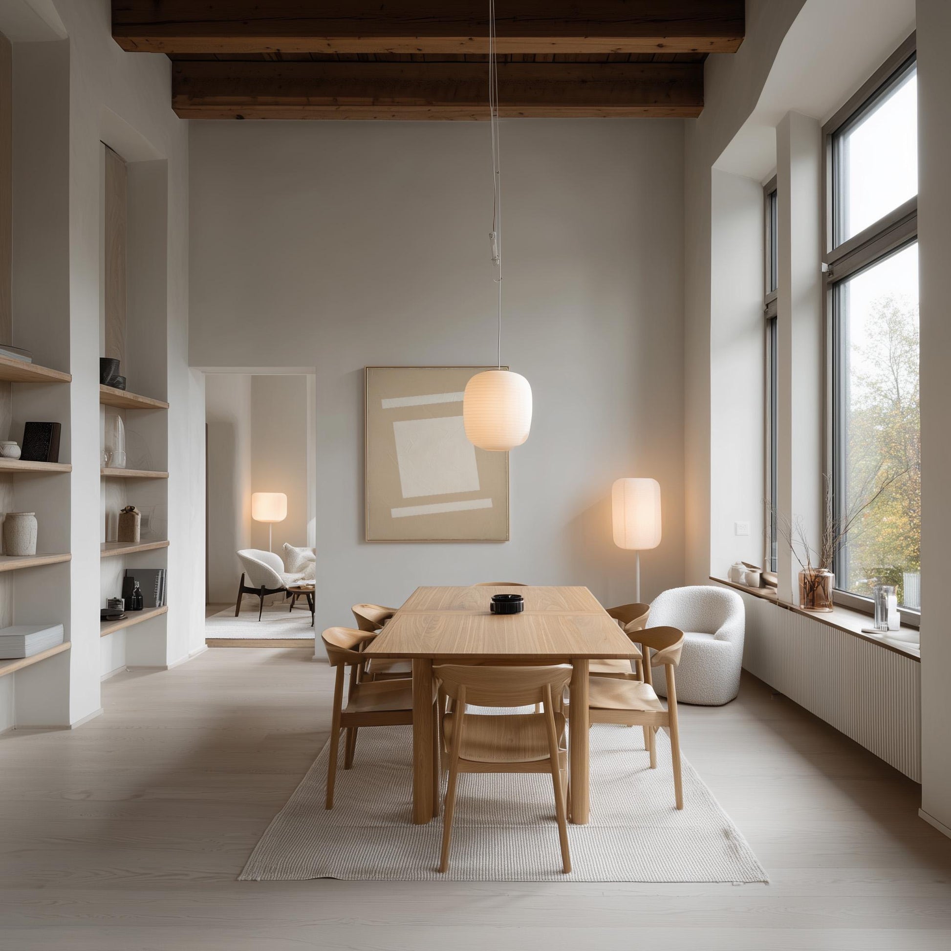 a modern and minimalist dining room with a large wooden table surrounded by matching chairs. The room features a high ceiling with exposed wooden beams, large windows that provide ample natural light, and a neutral color palette with white walls and light-colored furniture.