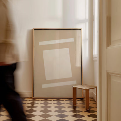 a large framed artwork hanging on a wall, with a small wooden stool placed in front of it. The room has a checkered floor and a window, creating a cozy and artistic atmosphere.