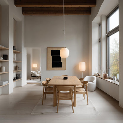 a modern and minimalist dining room with a large wooden table surrounded by matching chairs. The room features a high ceiling with exposed wooden beams, large windows that provide ample natural light, and a minimalist design with white walls and a white color scheme.