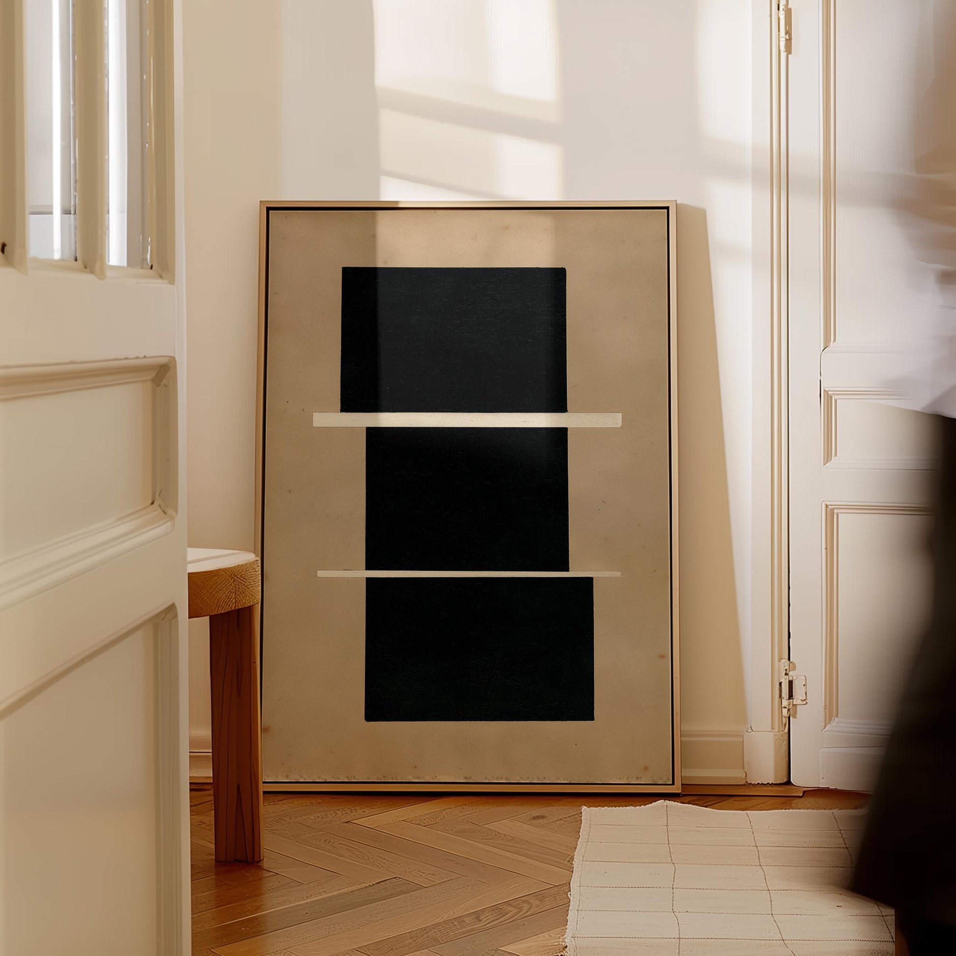 a large, abstract painting with a black background and three white rectangles arranged in a horizontal line. The painting is displayed on a white wall, and there is a wooden stool in the foreground.