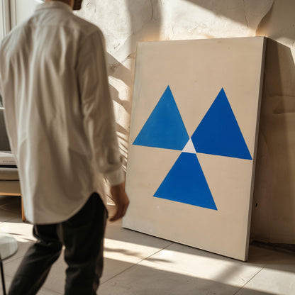 A person is standing in front of a large painting that features a blue triangle design.