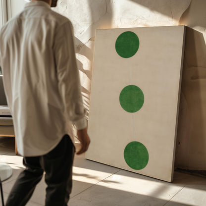 A person is standing in front of a large painting with three green circles on a white background.