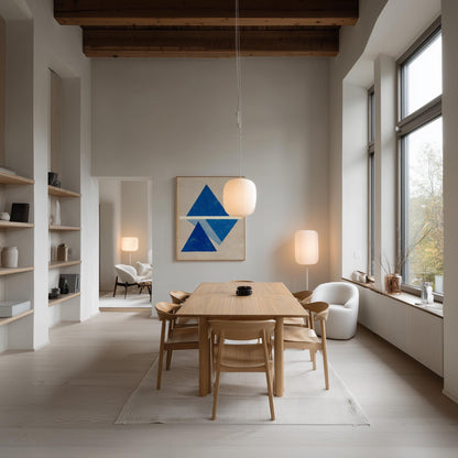a modern and minimalist dining room with a large wooden table surrounded by matching chairs. The room features a large window, a blue abstract painting on the wall, and various decorative elements such as lamps and vases.