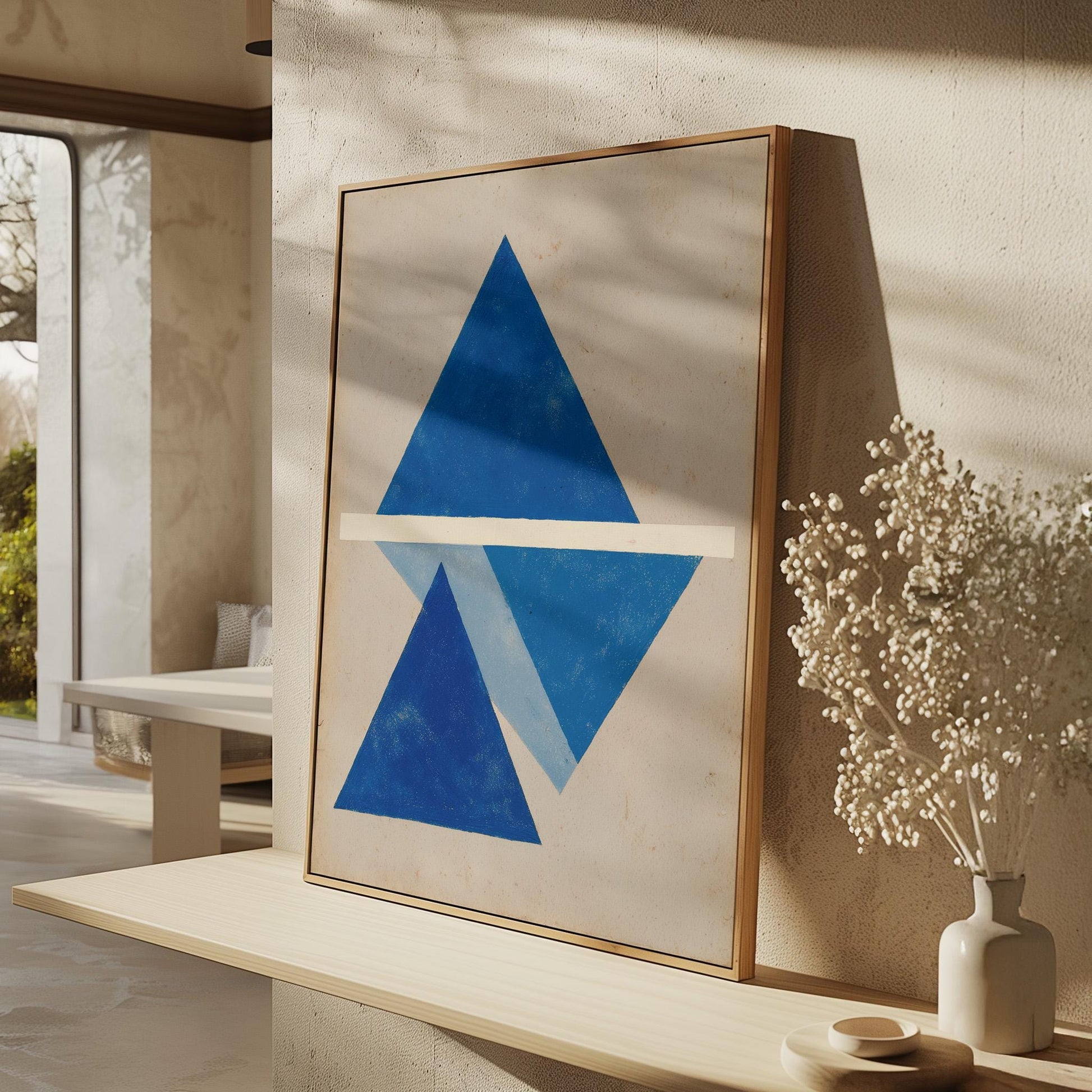 a large framed artwork with a blue triangle and a white line on a wall, accompanied by a vase of white flowers and a wooden shelf.