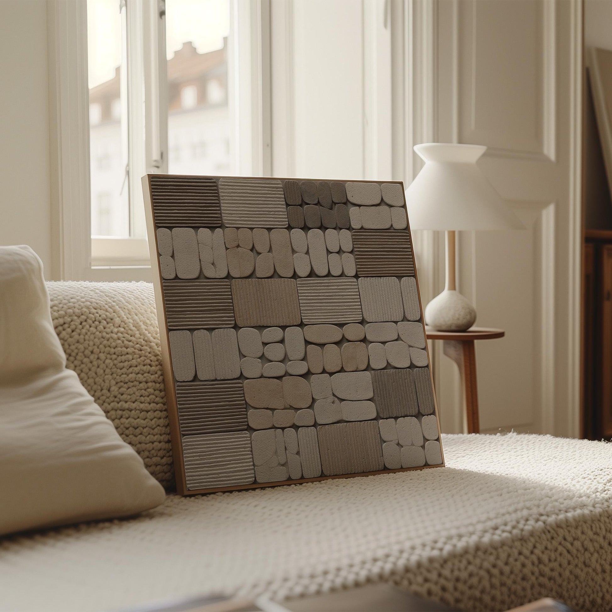 a large, square-shaped artwork with a geometric pattern of various shades of gray and white, displayed on a bed with a white blanket.