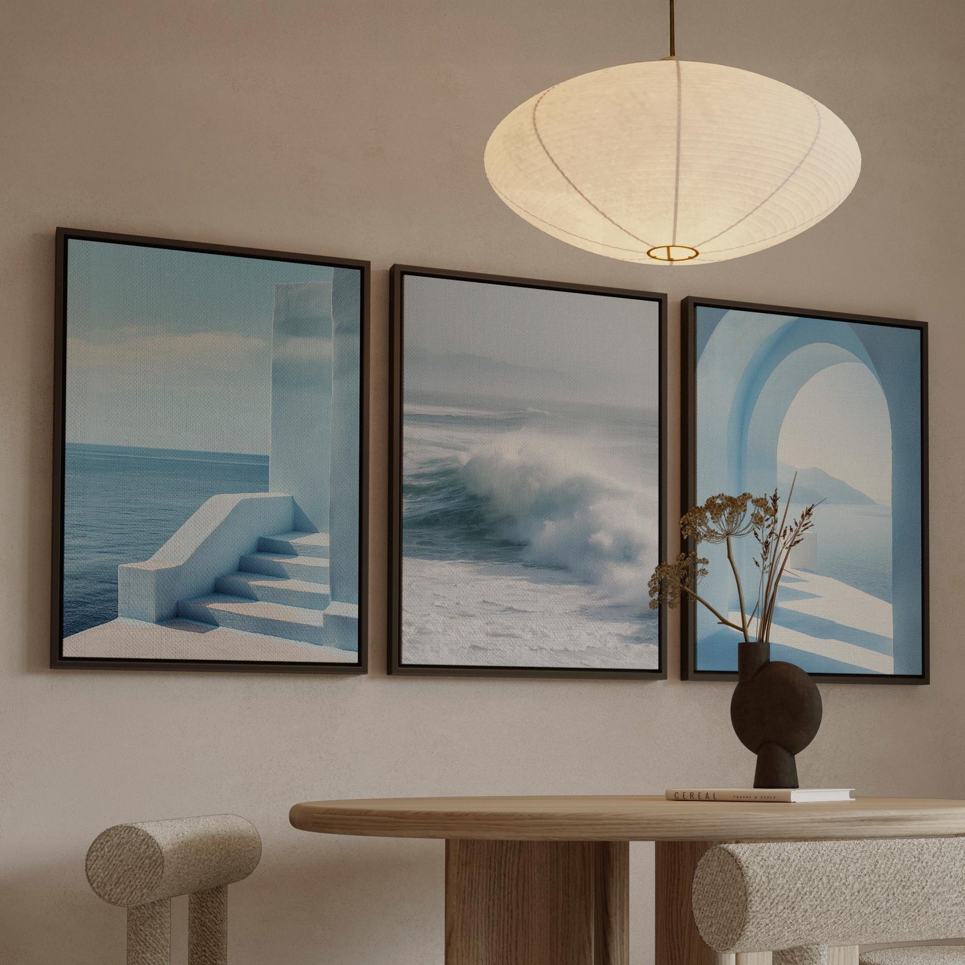 a modern dining room with a round wooden table, two white chairs, and three framed artworks displayed on the wall above the table.