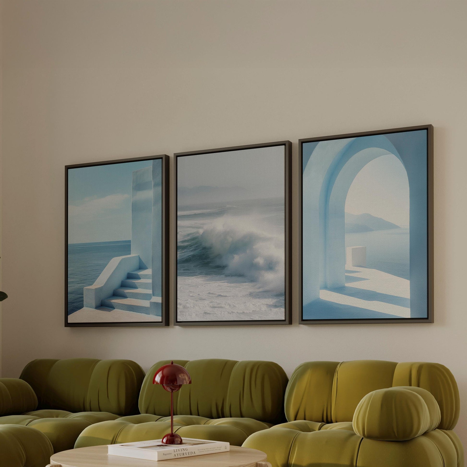 a living room with a green sofa and a red lamp on a table. Above the sofa, there are three framed pictures hanging on the wall, depicting a staircase, a wave, and an archway.