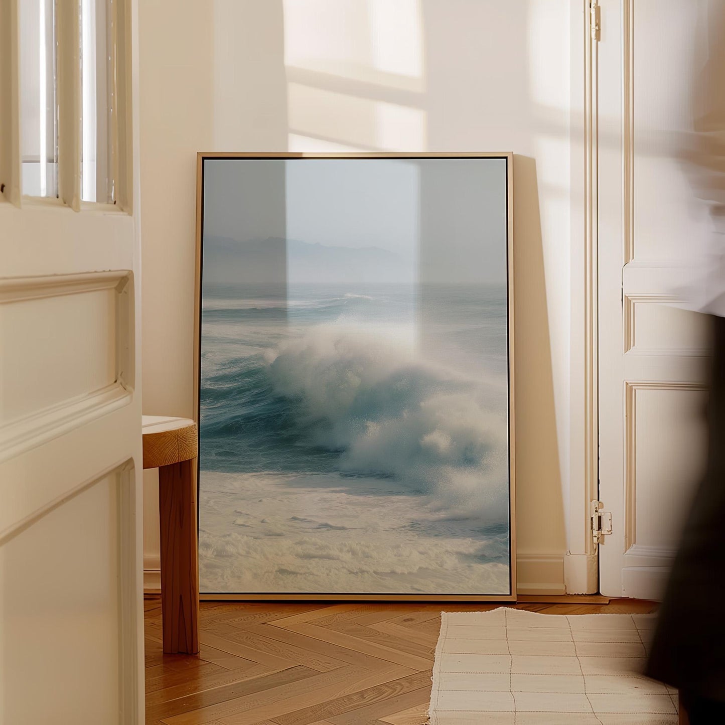 a large framed picture of a crashing wave, placed on a wooden floor in a room with a white door and a window.