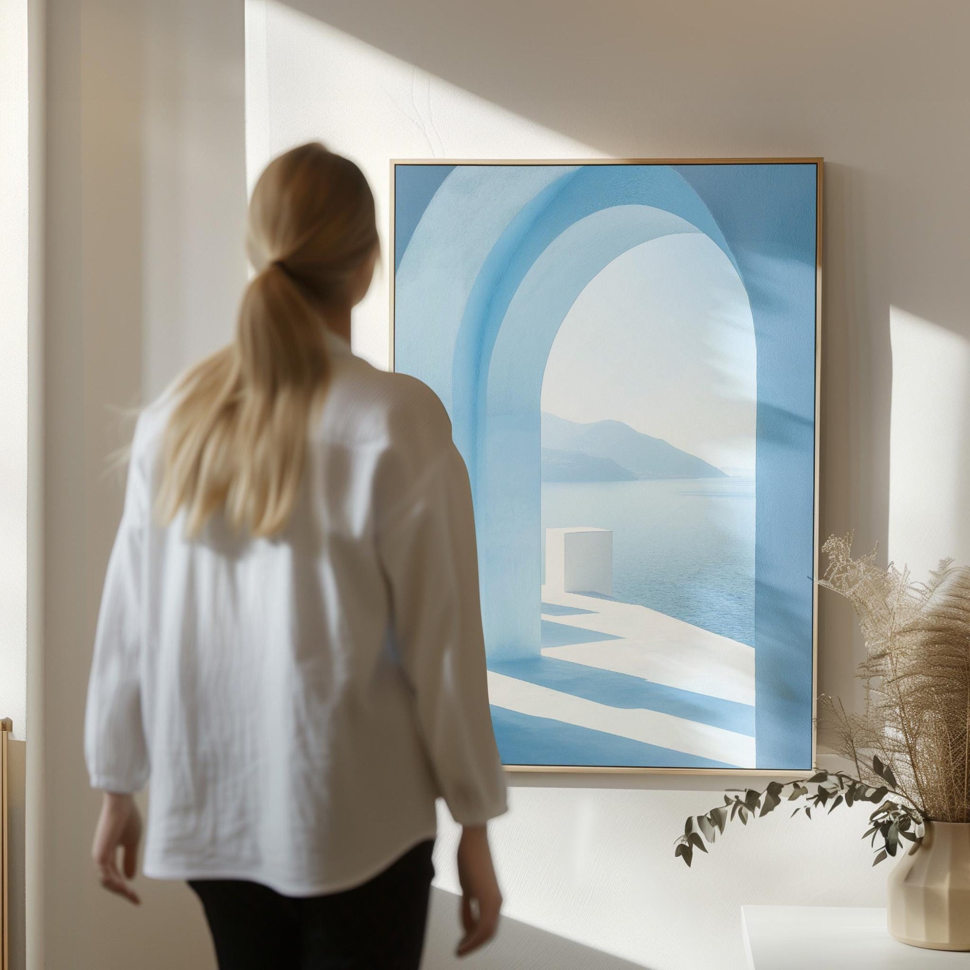 A woman in a white shirt stands in front of a large blue painting depicting an arched doorway leading to a serene landscape.