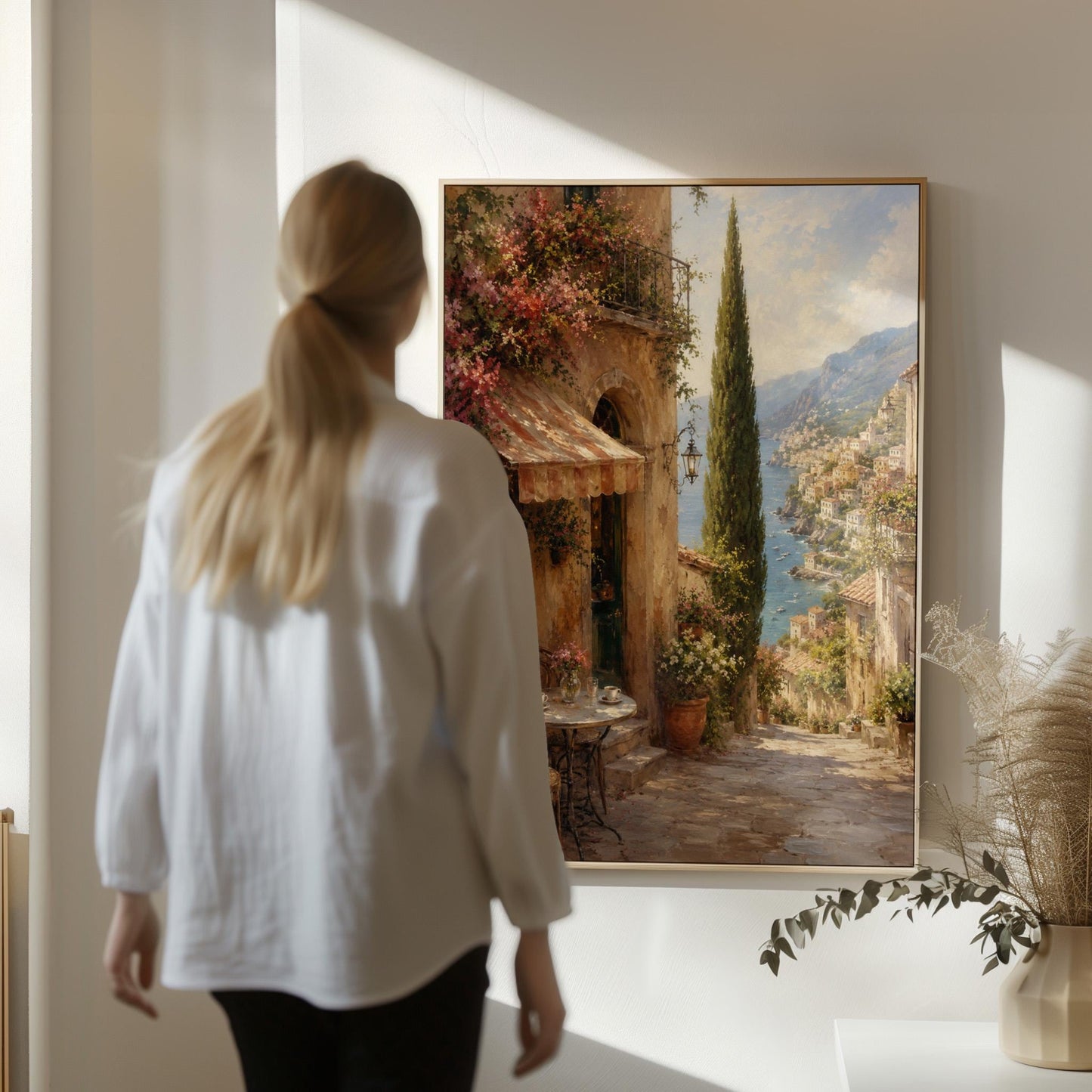 Italian village cafe painting with striped awning and coastal view, canvas print shown in a sunlit, contemporary room