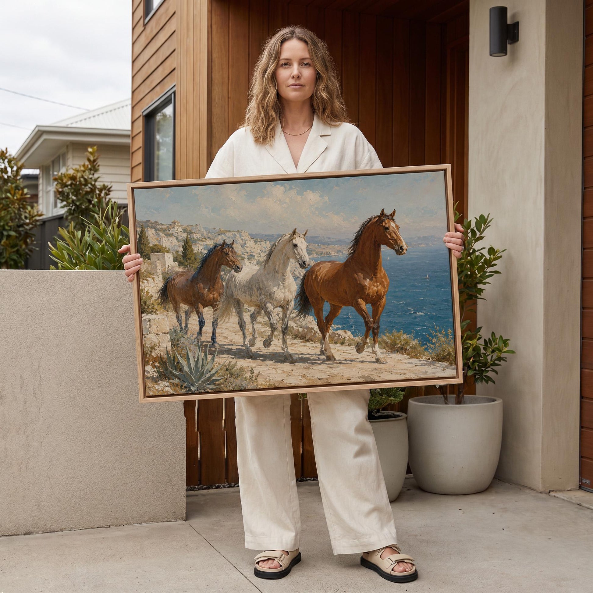 Three horses on a sunlit cliff above a blue Mediterranean bay, canvas wall art seen in a warm interior with natural light