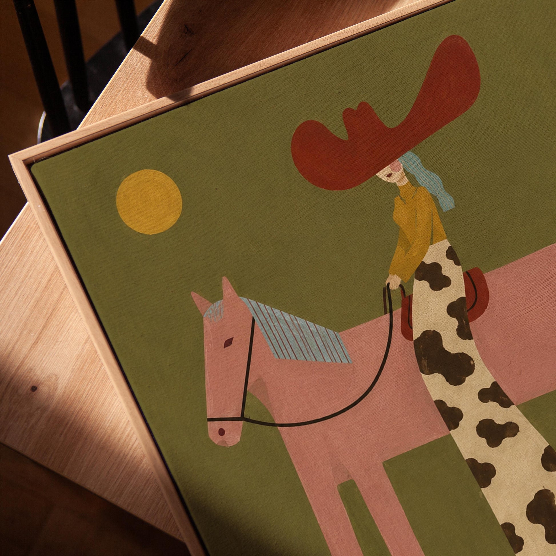 Cowgirl in a red hat riding a long-legged pink horse past a cactus at sunset, canvas print in a warm, minimally styled interior
