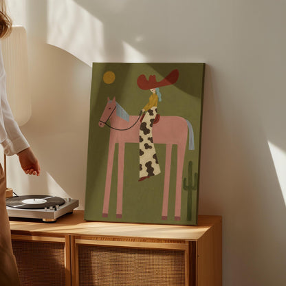 Cowgirl in a red hat riding a long-legged pink horse past a cactus at sunset, canvas wall art styled against a soft white wall