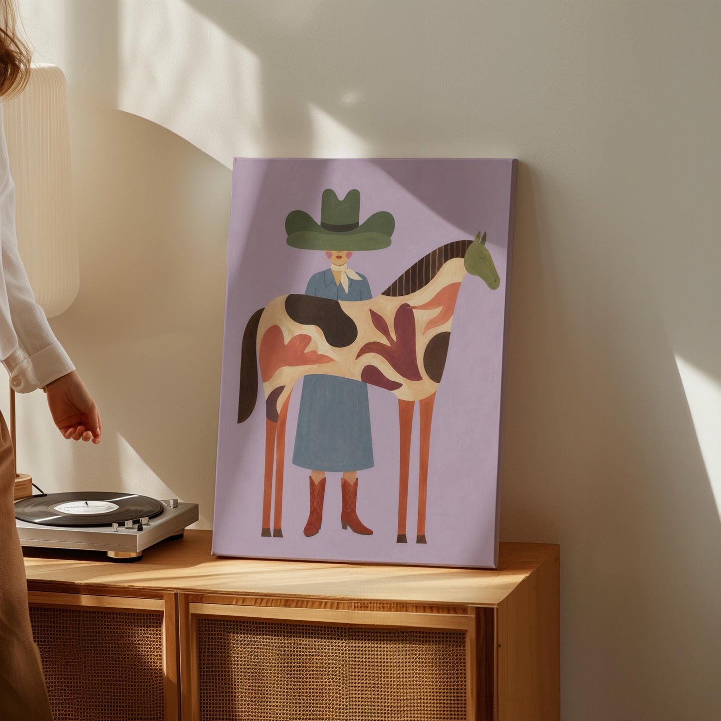Cowgirl in a green hat beside a tall patterned horse on soft lilac, canvas print styled against a soft white wall