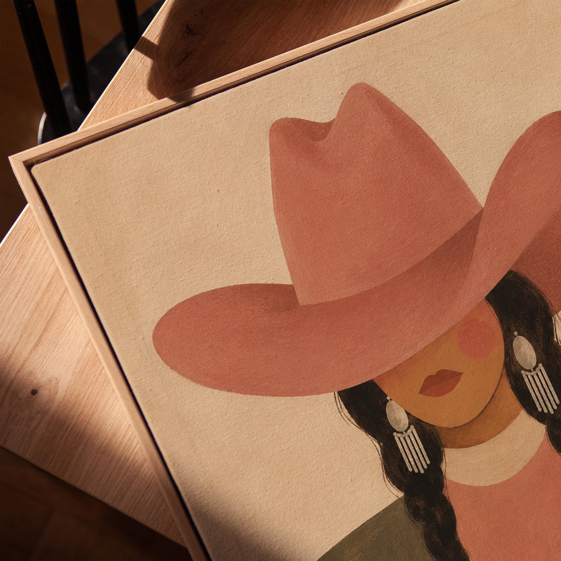 Cowgirl with dark braids under a wide terracotta hat and earthy western jacket, canvas print in a warm, minimally styled interior