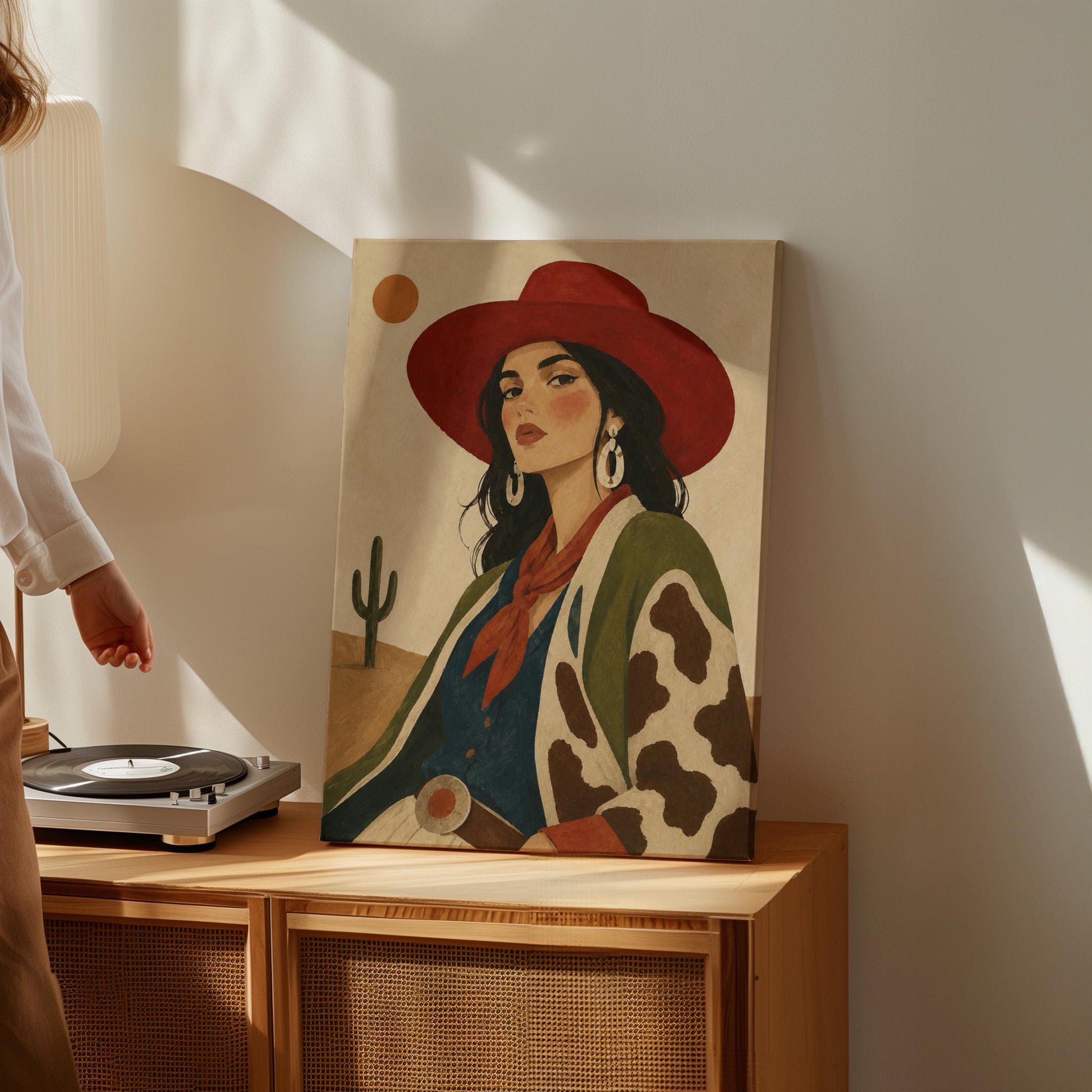 Dark-haired cowgirl in a red hat and cow-print jacket before a desert cactus, canvas wall art on a quiet wall in a considered interior