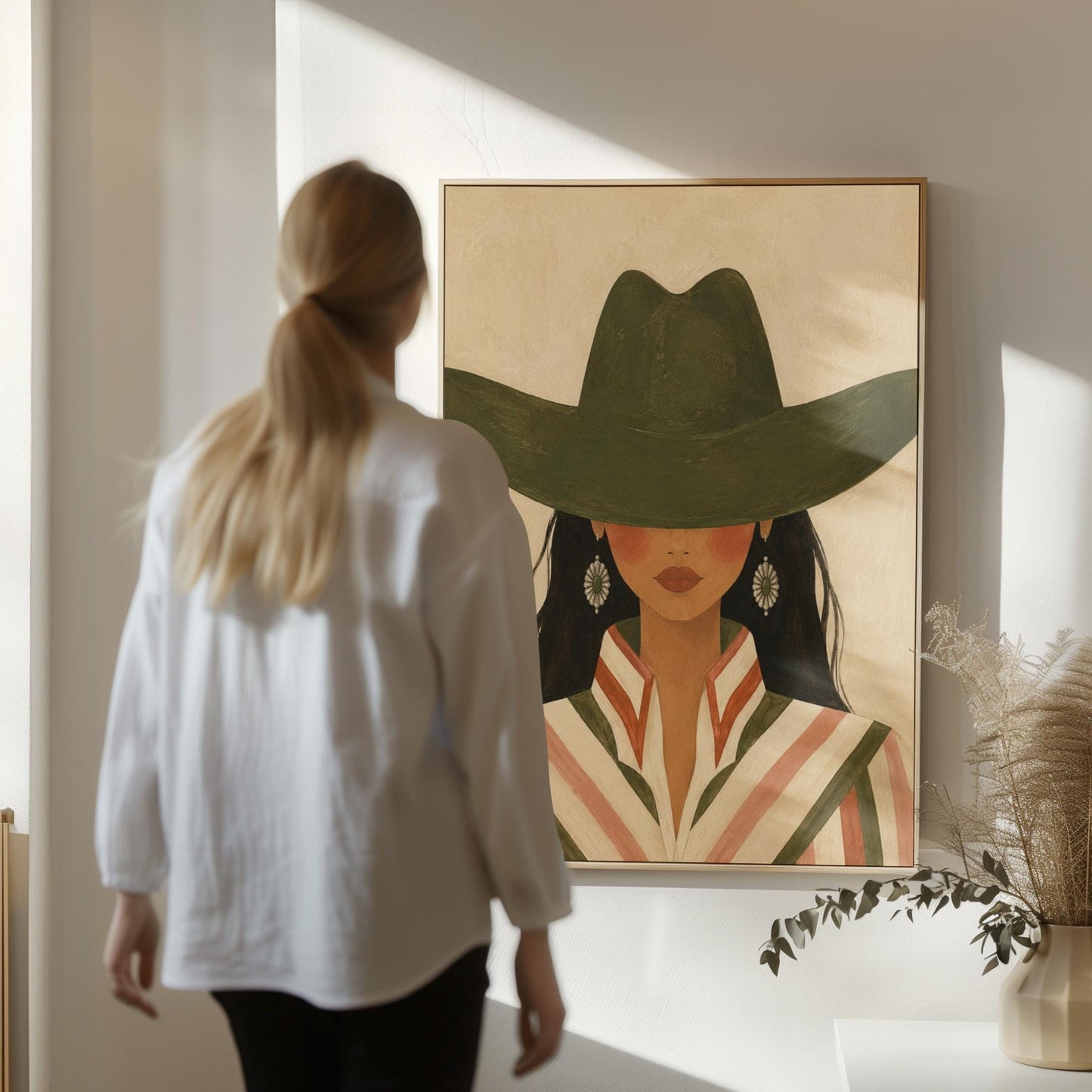Cowgirl under a deep green hat with concho earrings and a striped western shirt, canvas print shown to scale in a furnished room