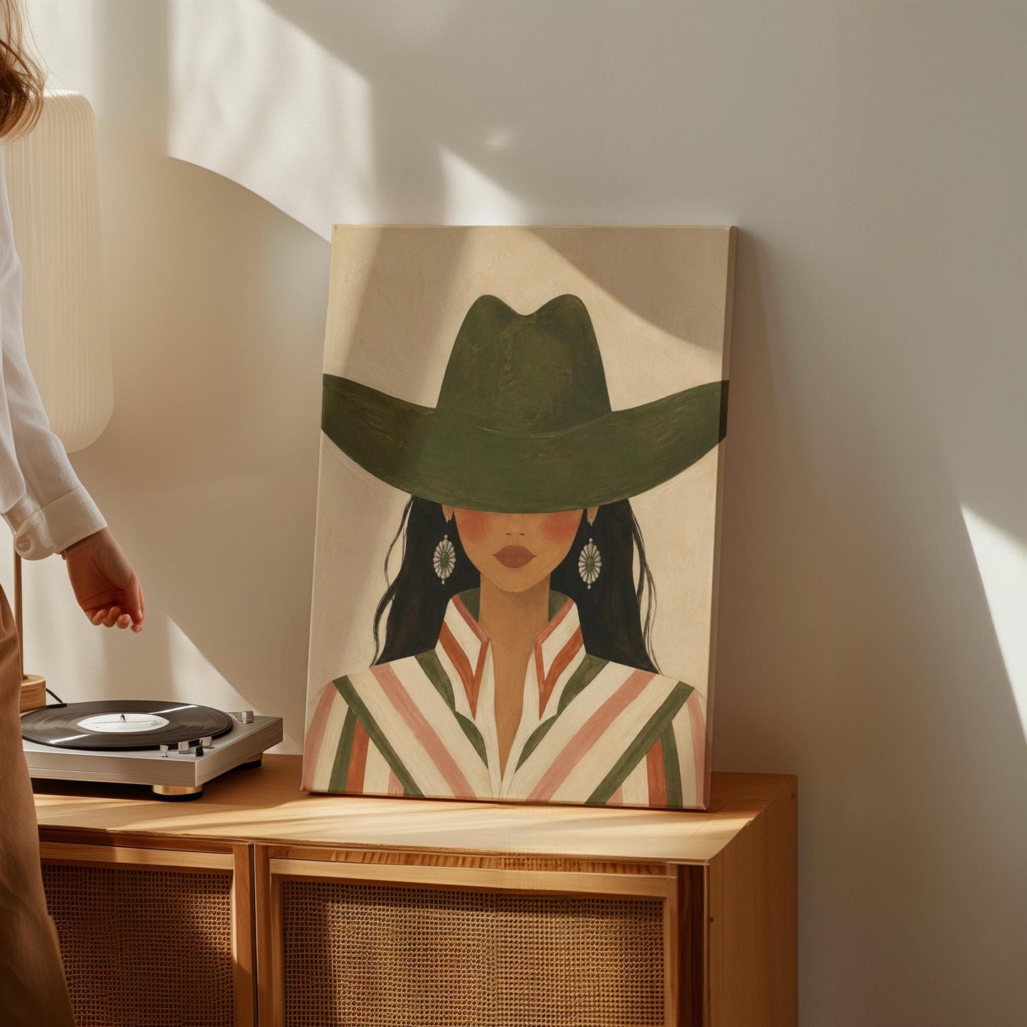 Cowgirl under a deep green hat with concho earrings and a striped western shirt, canvas print displayed on a neutral wall in a styled interior
