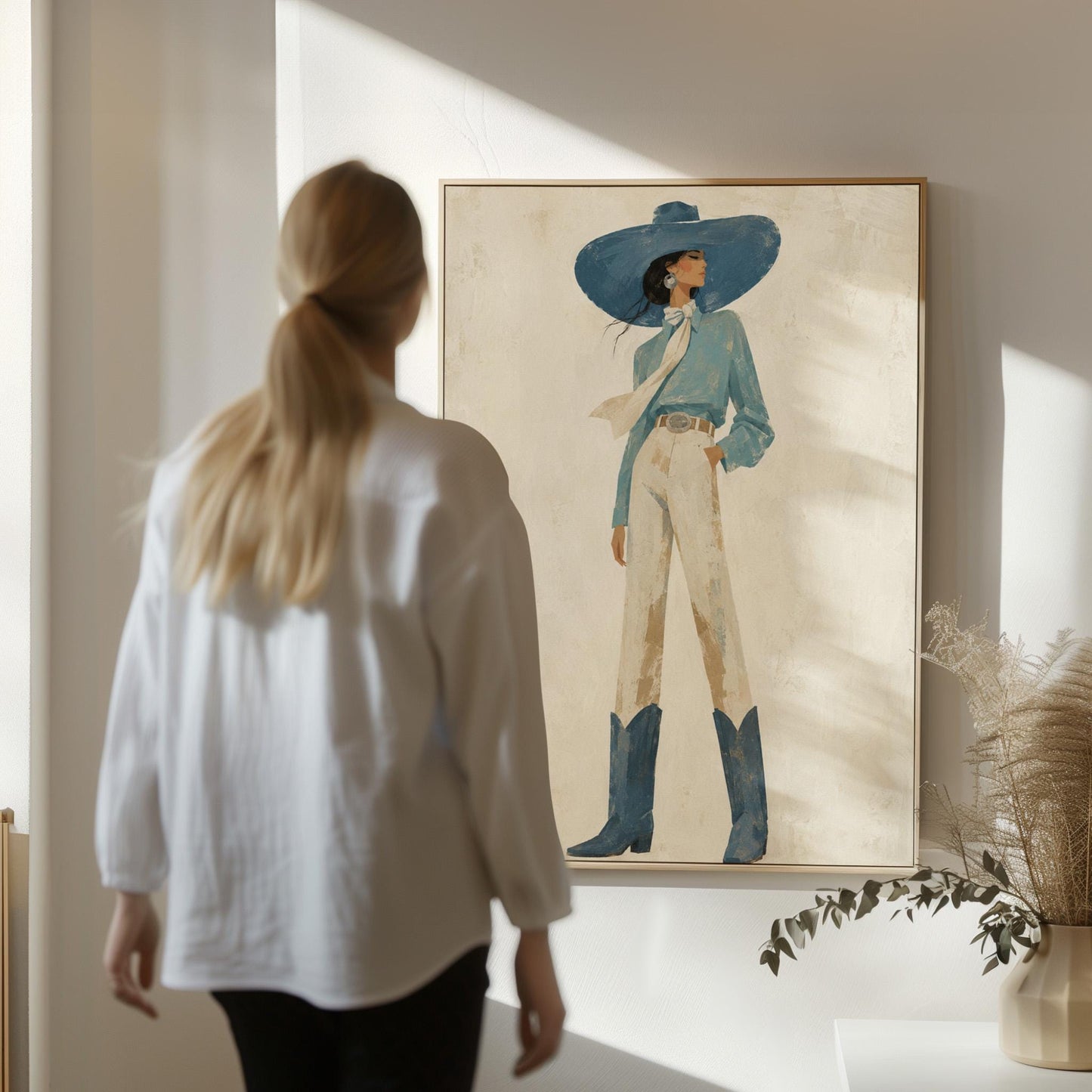 Full-figure cowgirl in a wide teal hat, blouse and boots with cream trousers, canvas print styled against a soft white wall
