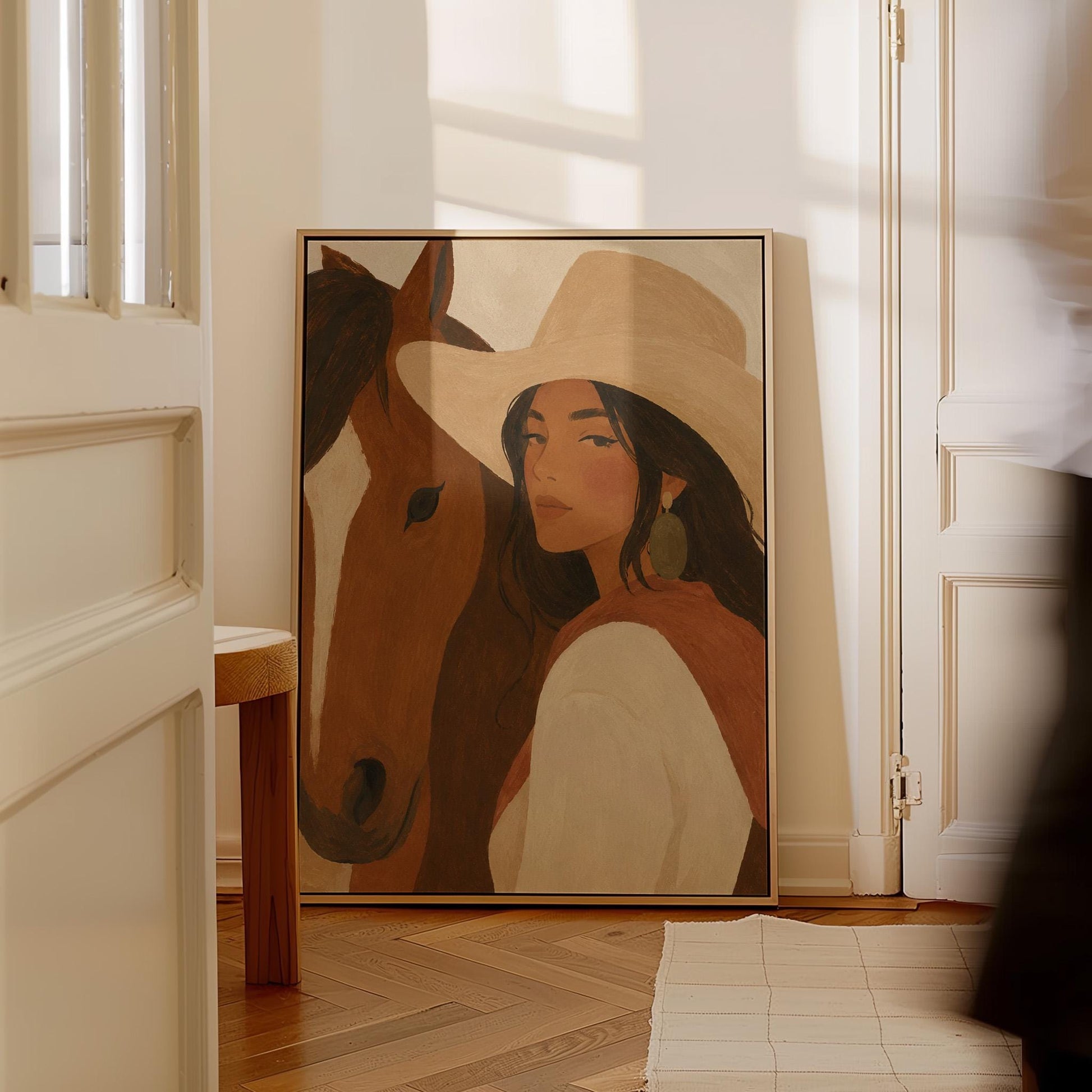 Cowgirl in a cream hat leaning cheek to cheek with a chestnut horse on warm tan, canvas wall art presented in a light, minimal room