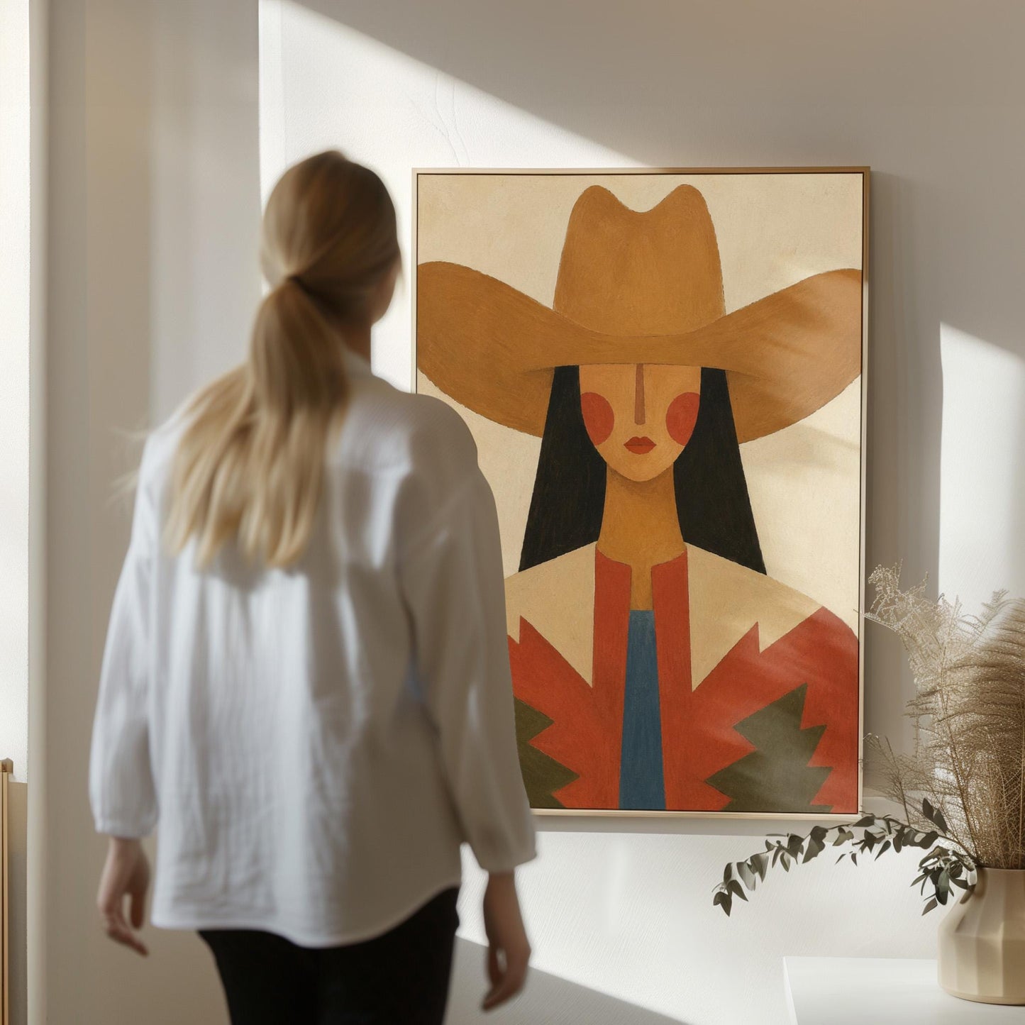 Folk cowgirl in a tan hat with rosy cheeks and a red aztec jacket on cream, canvas print hanging in a calm, modern living space