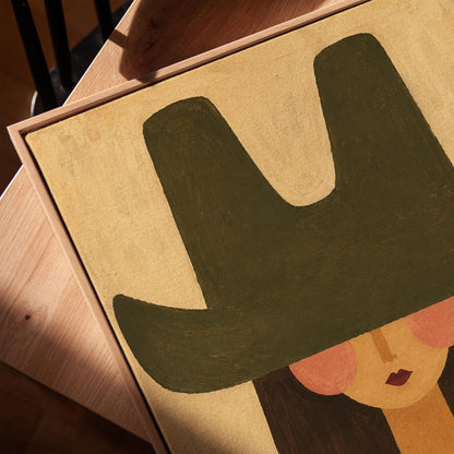 Folk cowgirl in a big green hat and striped shirt with long dark hair, canvas print in a warm, minimally styled interior