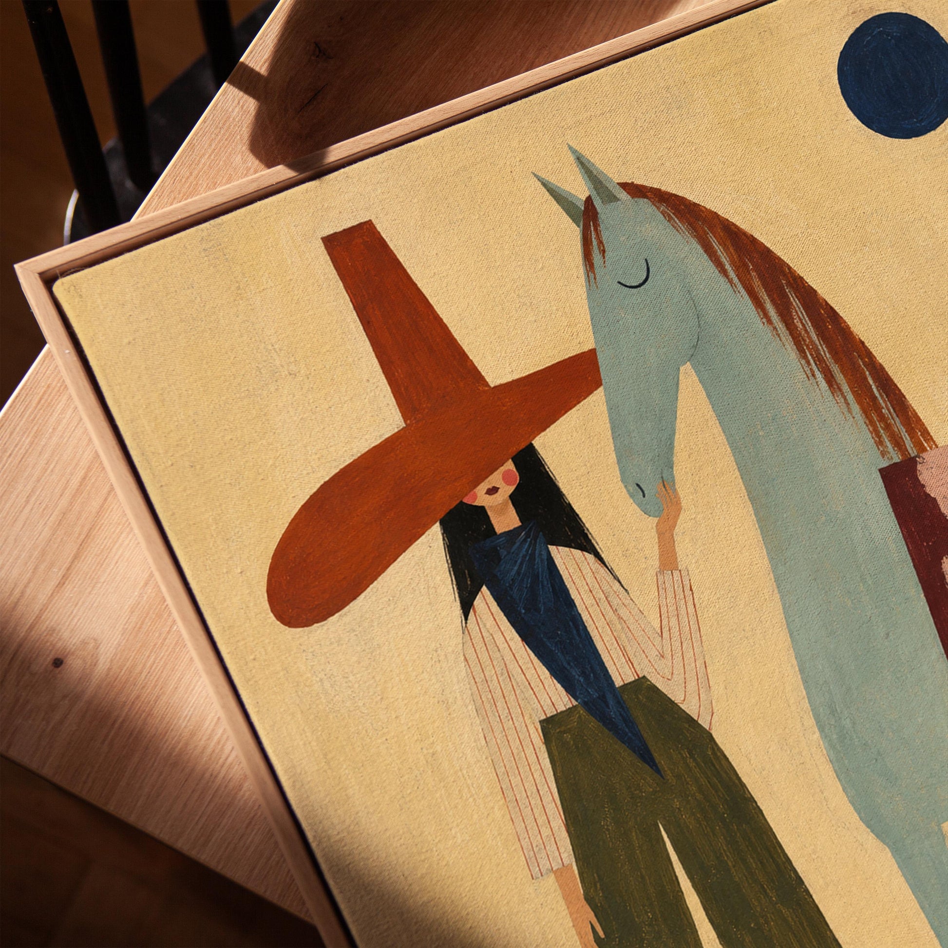 Woman in a wide red hat standing beside a gentle blue horse in the desert, canvas print in a warm, minimally styled interior