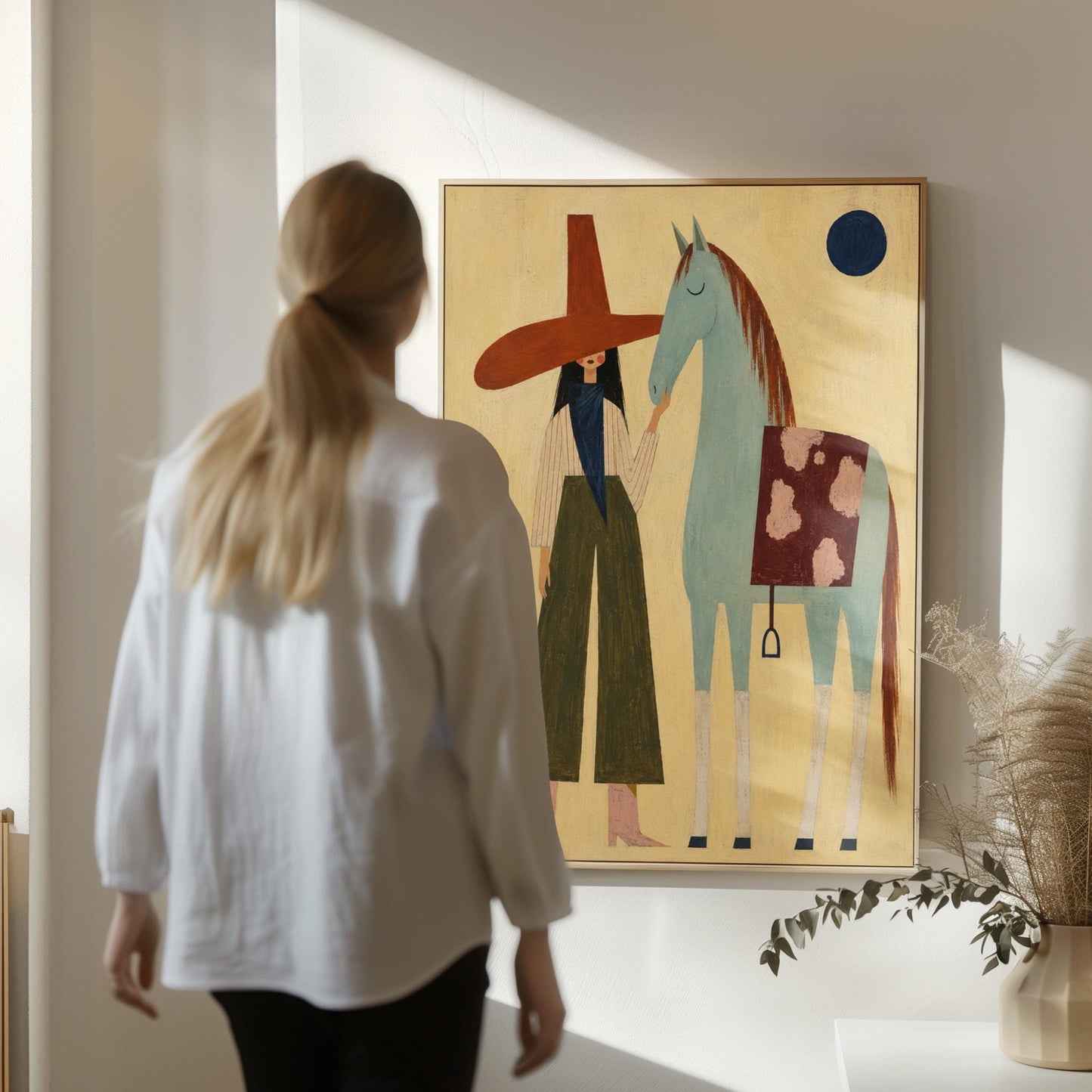 Woman in a wide red hat standing beside a gentle blue horse in the desert, canvas print shown to scale in a furnished room