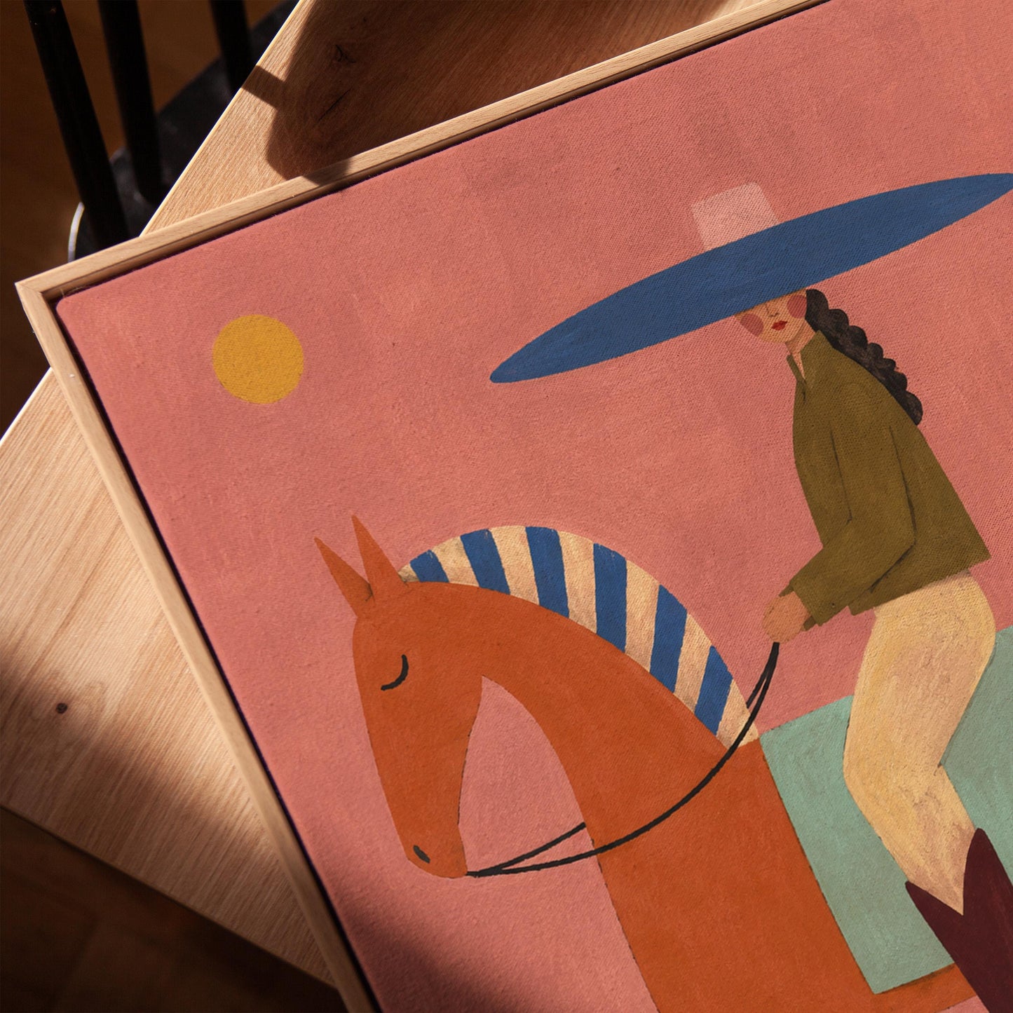 Cowgirl in a broad blue hat riding a rust red horse across a coral sky, canvas print in a warm, minimally styled interior