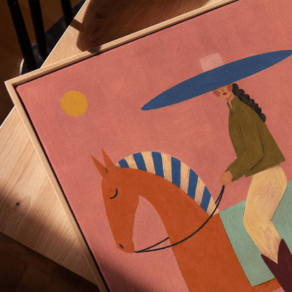 Cowgirl in a broad blue hat riding a rust red horse across a coral sky, canvas print in a warm, minimally styled interior