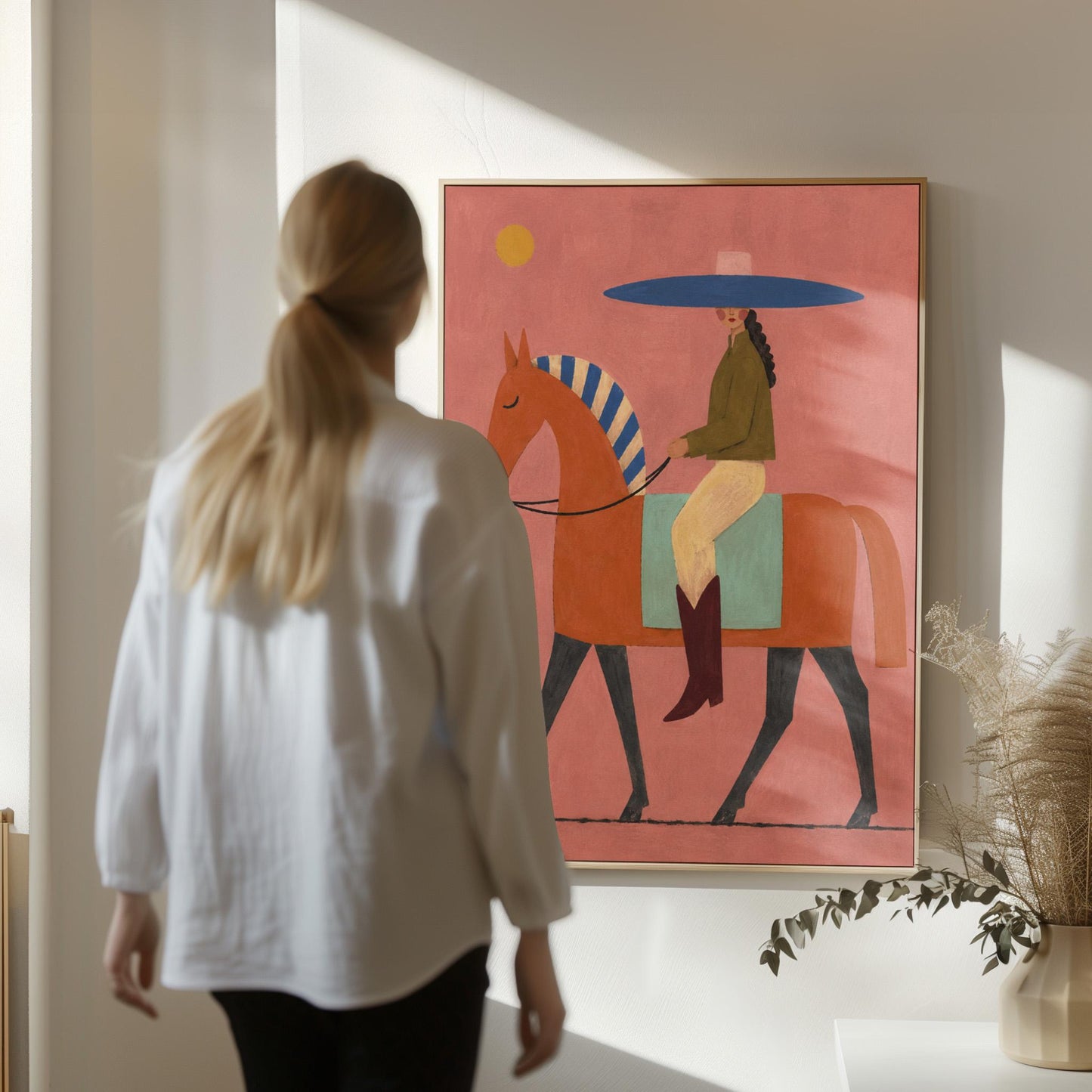 Cowgirl in a broad blue hat riding a rust red horse across a coral sky, canvas print seen in a warm interior with natural light