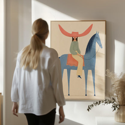 Cowgirl in a dramatic red hat riding a slender blue horse across pale sand, canvas print presented in a light, minimal room