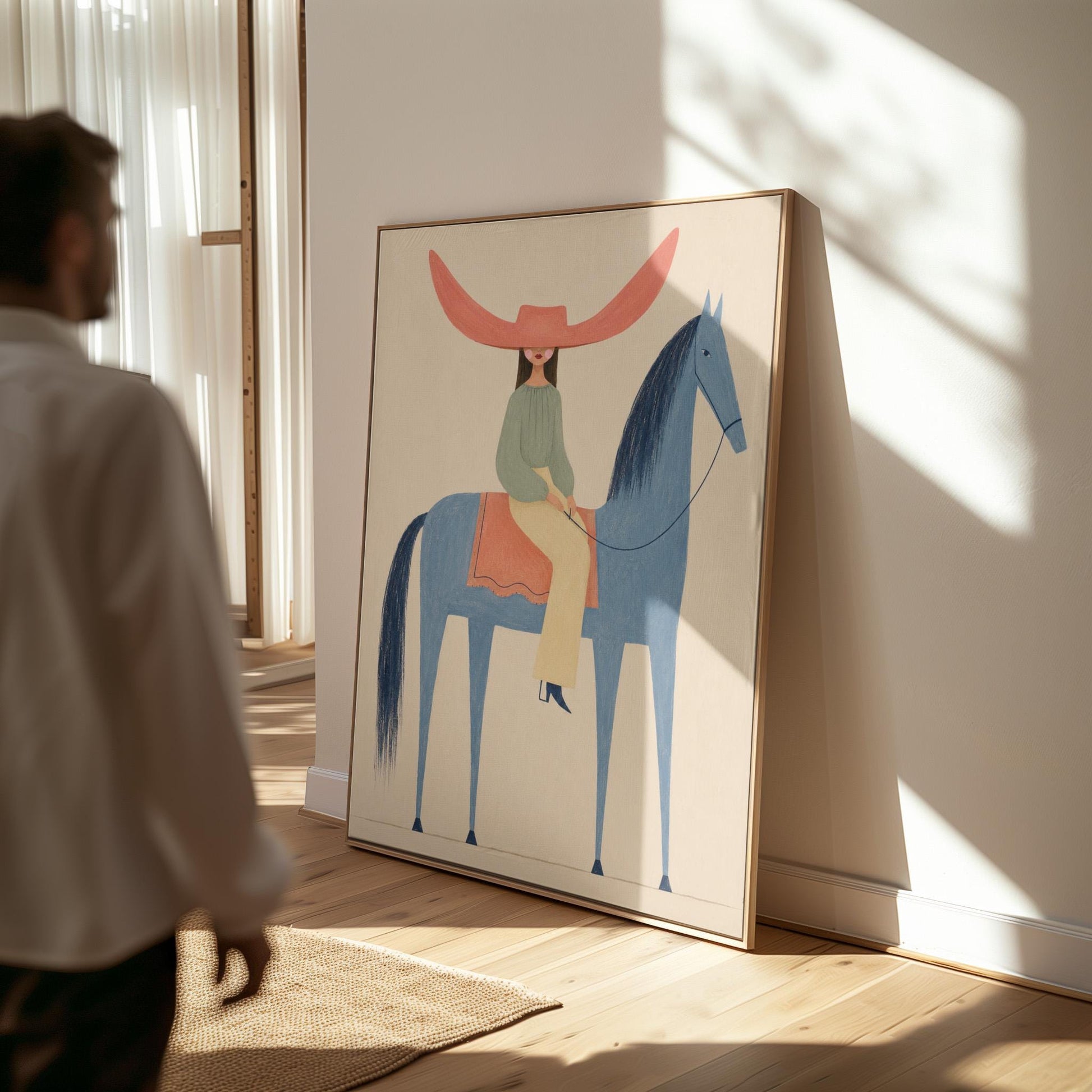 Cowgirl in a dramatic red hat riding a slender blue horse across pale sand, canvas print shown to scale in a furnished room