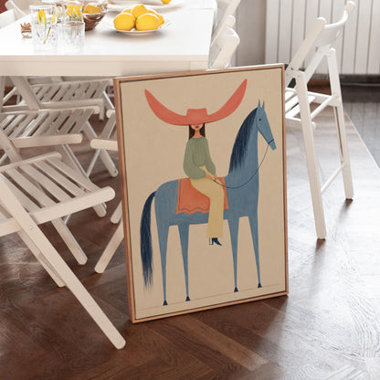 Cowgirl in a dramatic red hat riding a slender blue horse across pale sand, canvas print displayed on a neutral wall in a styled interior