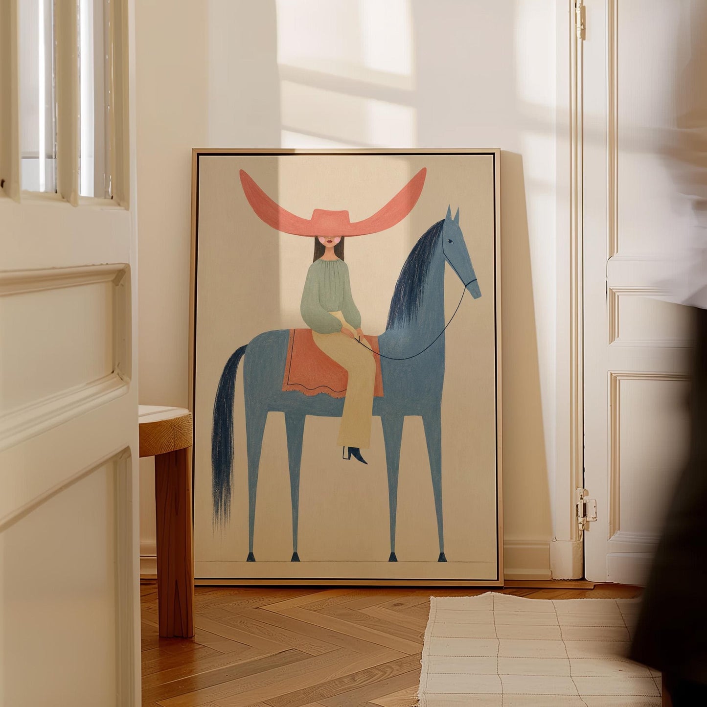 Cowgirl in a dramatic red hat riding a slender blue horse across pale sand, canvas print seen in a warm interior with natural light