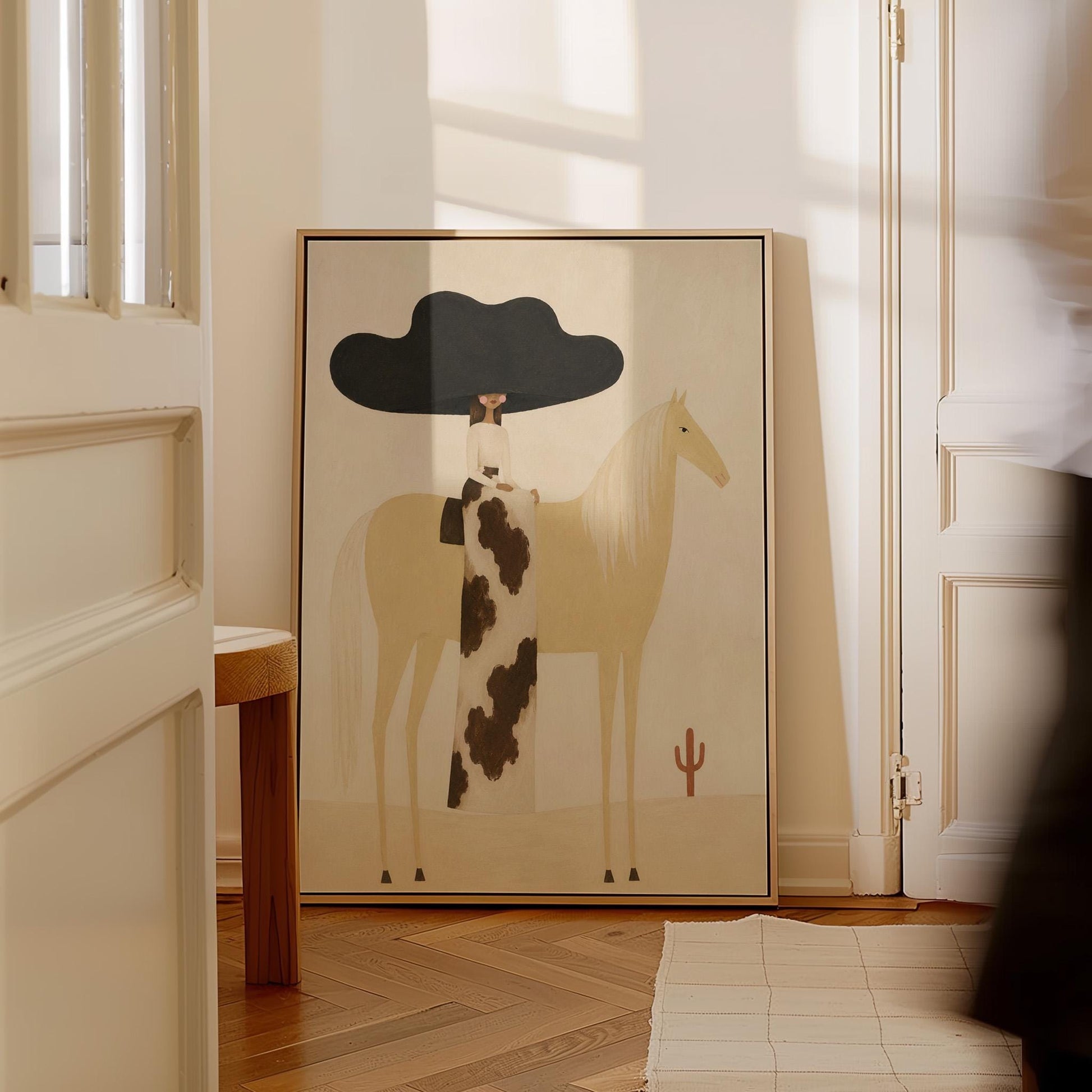 Woman in a huge black hat riding a pale palomino across a desert with cactus, canvas print seen in a warm interior with natural light