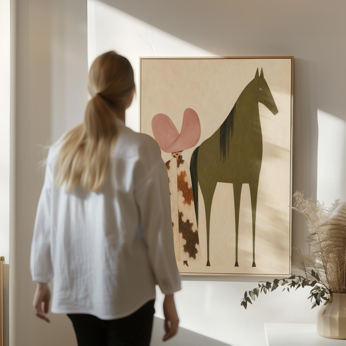 Cowgirl in a green hat and spotted pants before a deep maroon folk horse, canvas print presented in a light, minimal room