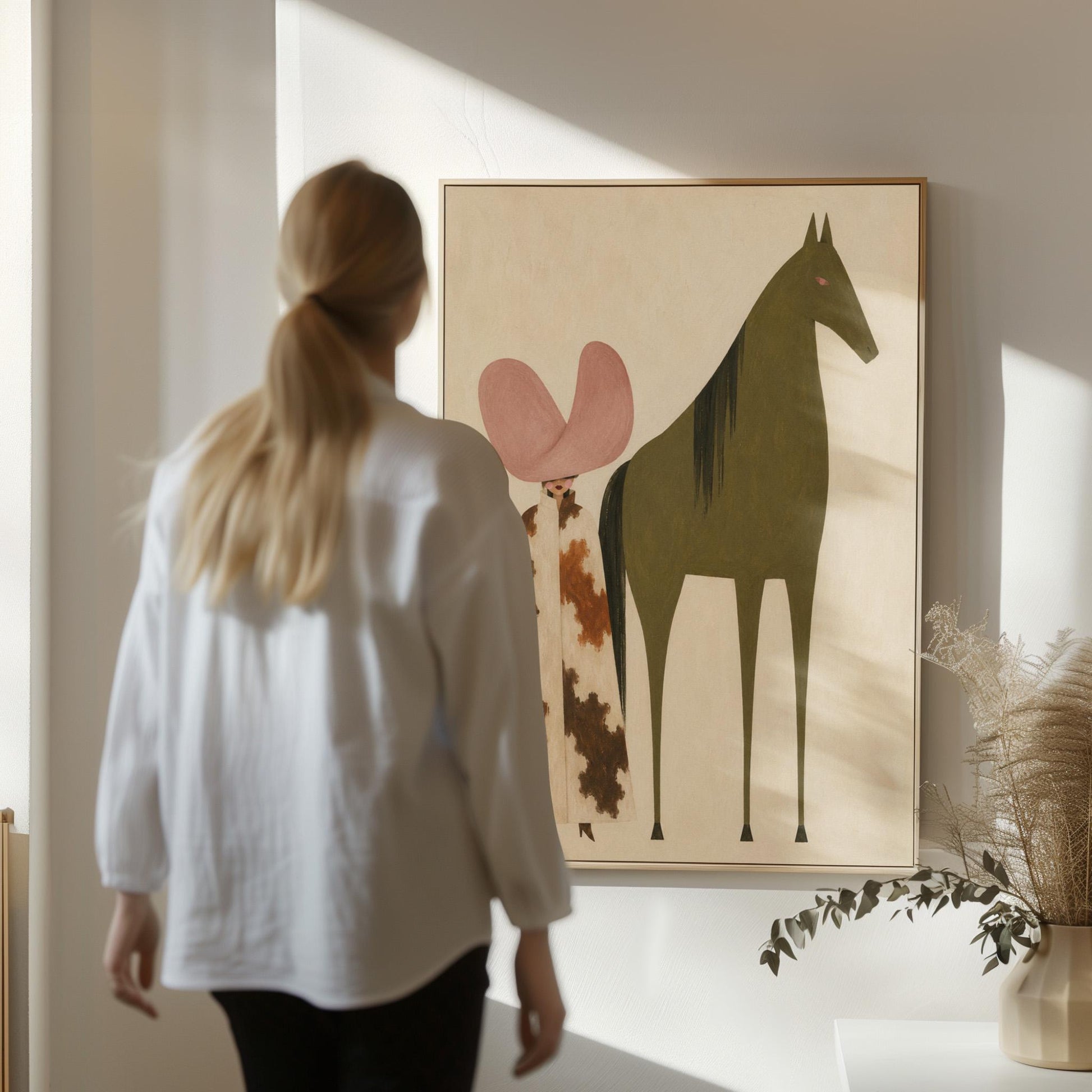 Cowgirl in a green hat and spotted pants before a deep maroon folk horse, canvas print presented in a light, minimal room